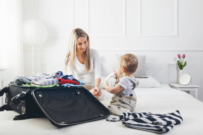 Travelling with kids. Happy mother with her child packing clothes for holiday